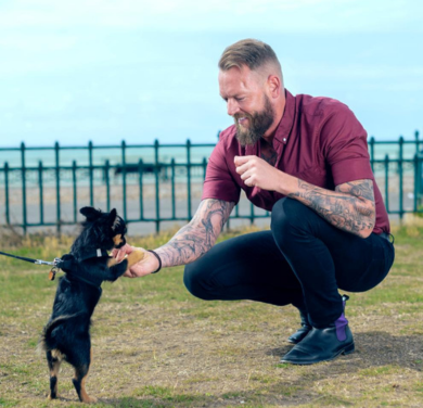 A man crouched down feeding a small dog