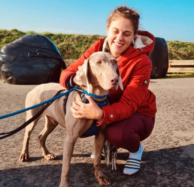A woman knelt down smiling at a grey dog