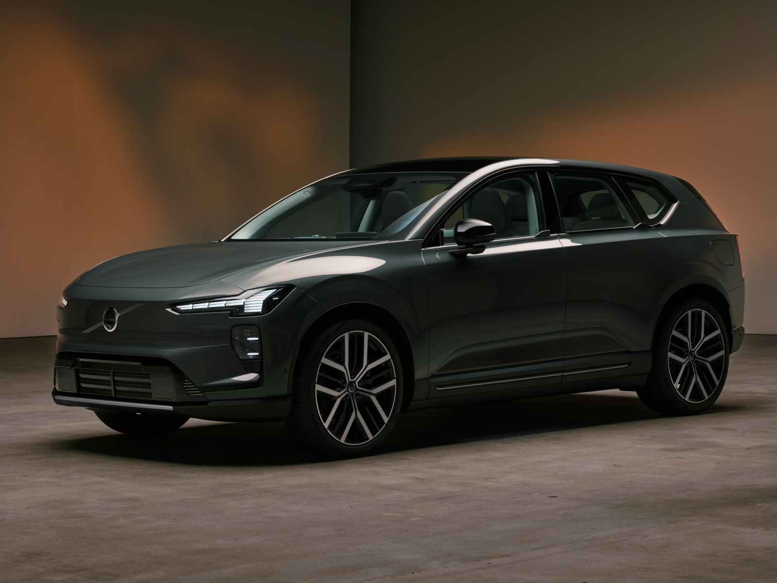 A black Volvo EX60 car in front of a brown background