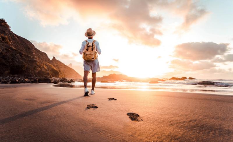 man walking on a beach with a backpack on