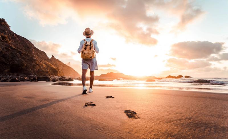 man walking on a beach with a backpack on 