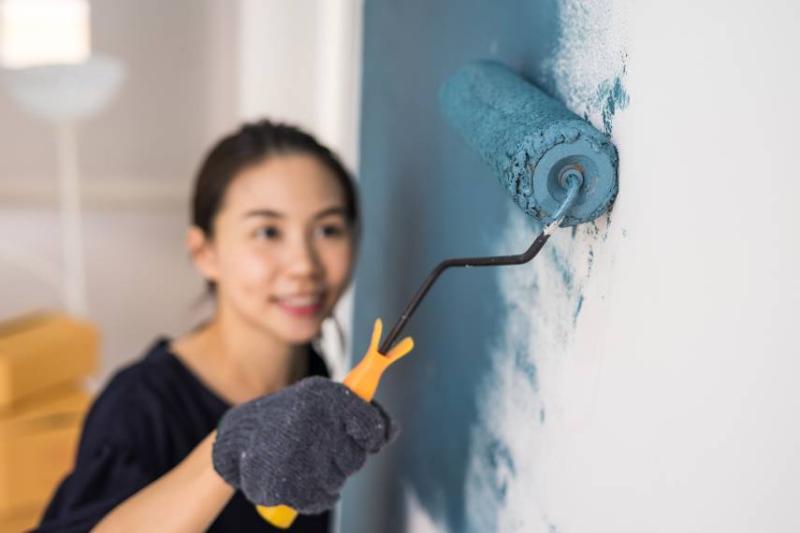 Image of an Asian woman painting the wall teal
