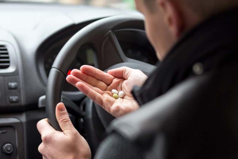 Image of a man looking at pills before driving.
