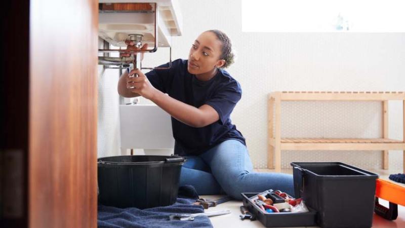 Image of a woman plumber finding and fixing a leak.