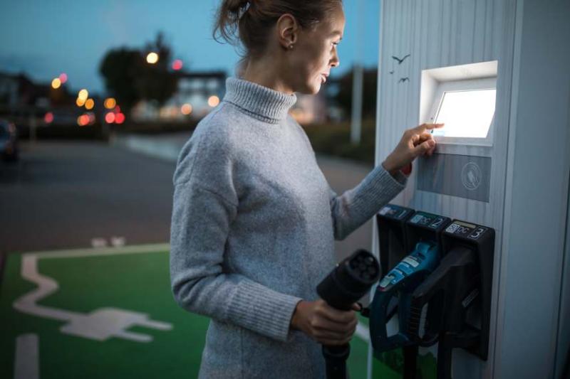 Image of a white woman charging her EV. 