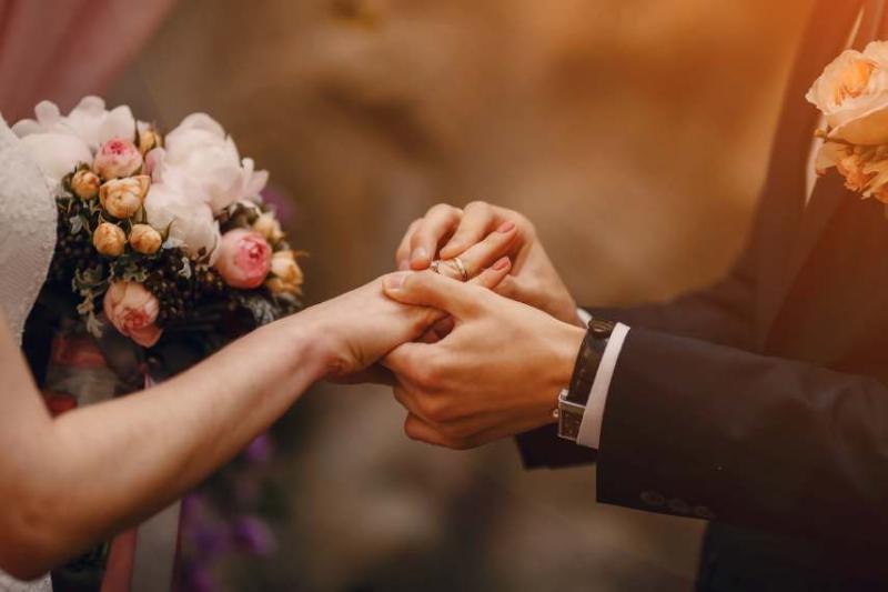 A man putting a ring on a woman's finger holding a wedding bouquet