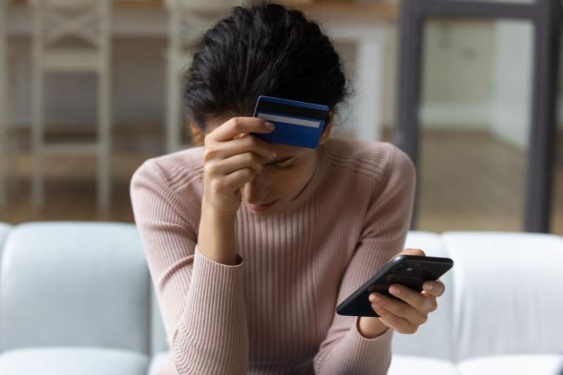 Woman with head in hands holding a credit card and her phone