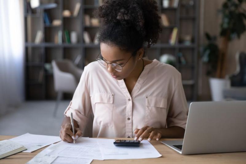 A young woman sat at a table budgeting with her laptop and calculator