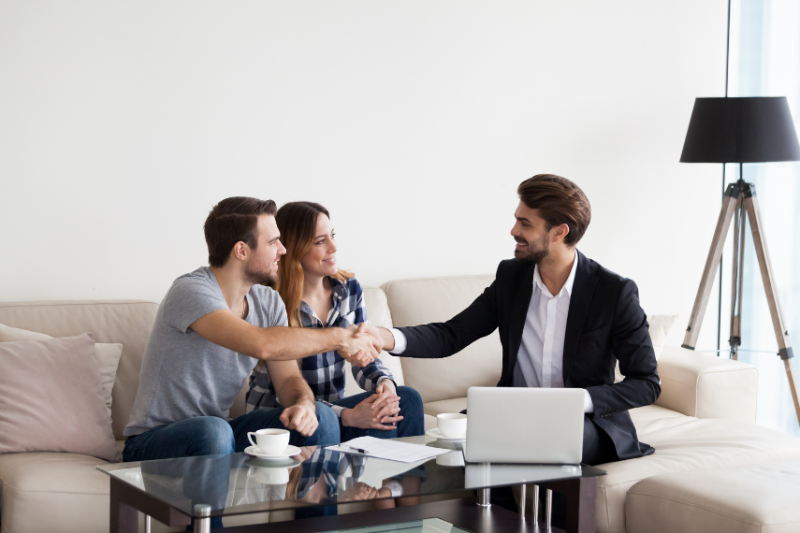 Man handing a set of keys to a couple, sat on sofa
