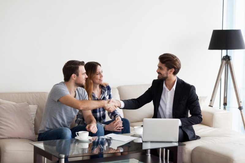 Man handing a set of keys to a couple, sat on sofa 