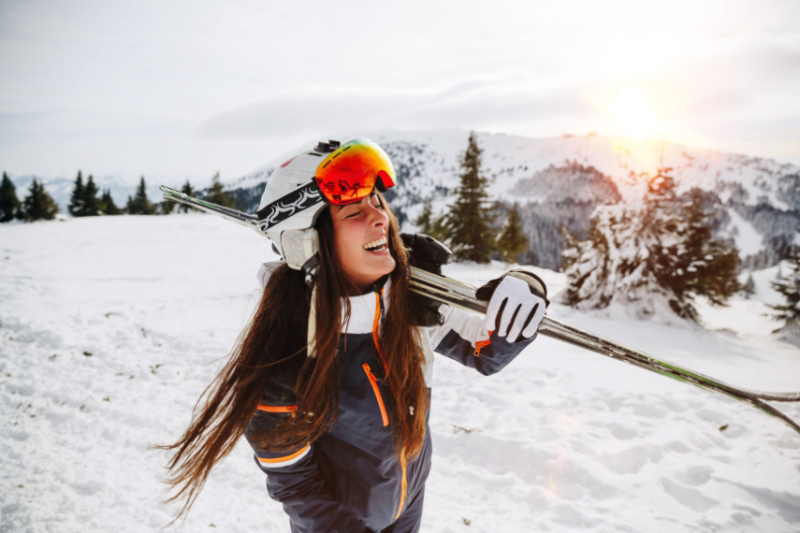 A woman holding her skis over her shoulder on a ski slope and smiling