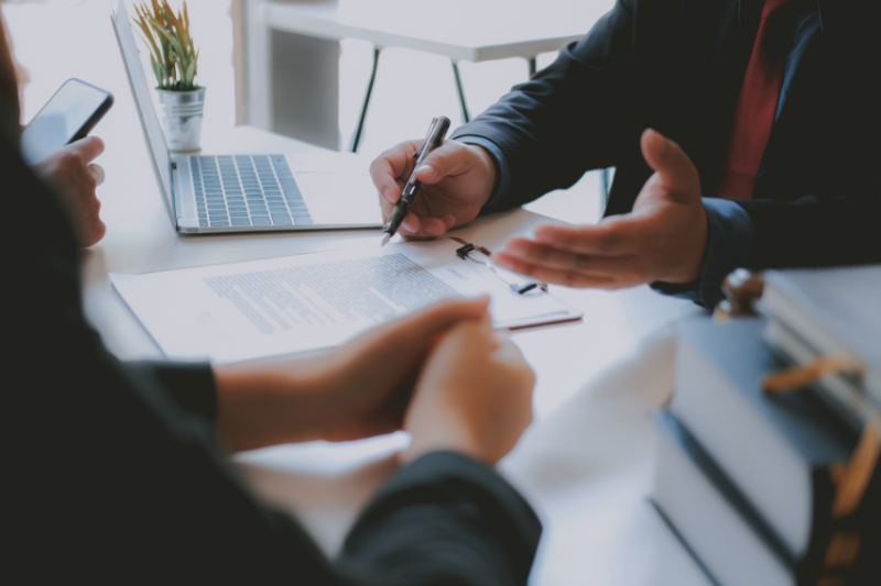 Shot of a desk with laptop and contract and two people speaking over it