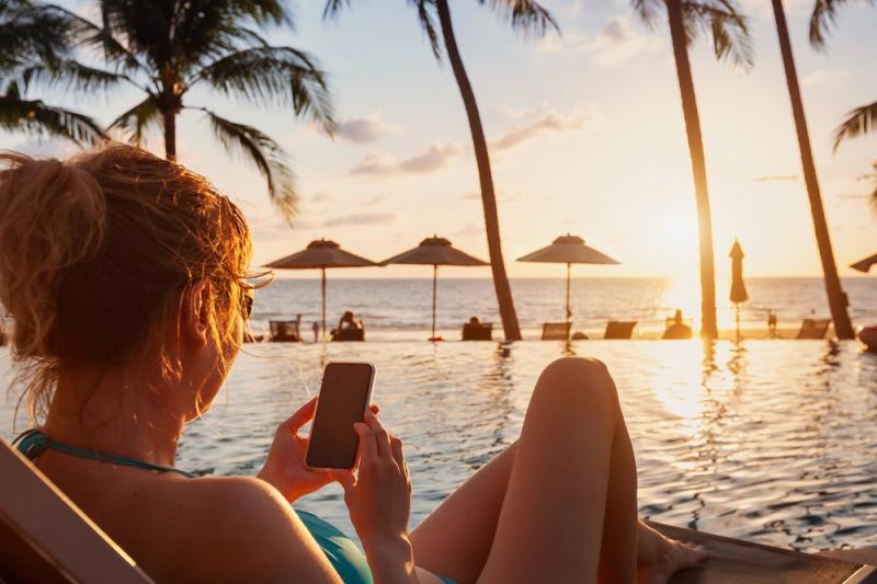 Woman using mobile phone on beach luxury hotel near swimming pool sunset