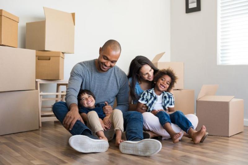 Family of four sitting on floor of house surrounded by boxes