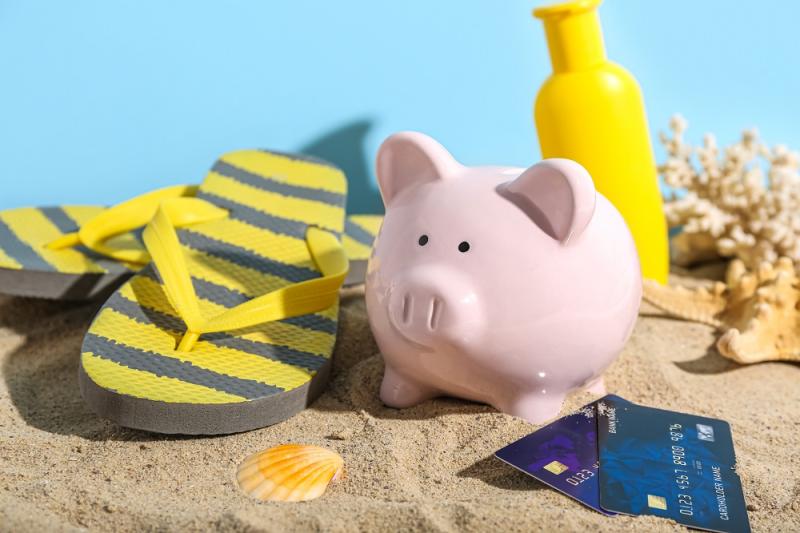 Piggy bank with beach accessories, sunscreen cream and credit cards on sand 