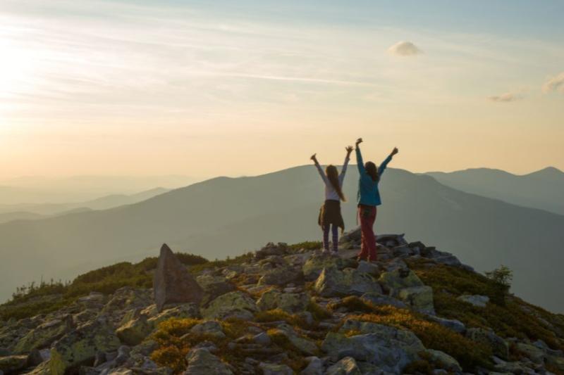 Mother and child on top of mountain with their arms up 