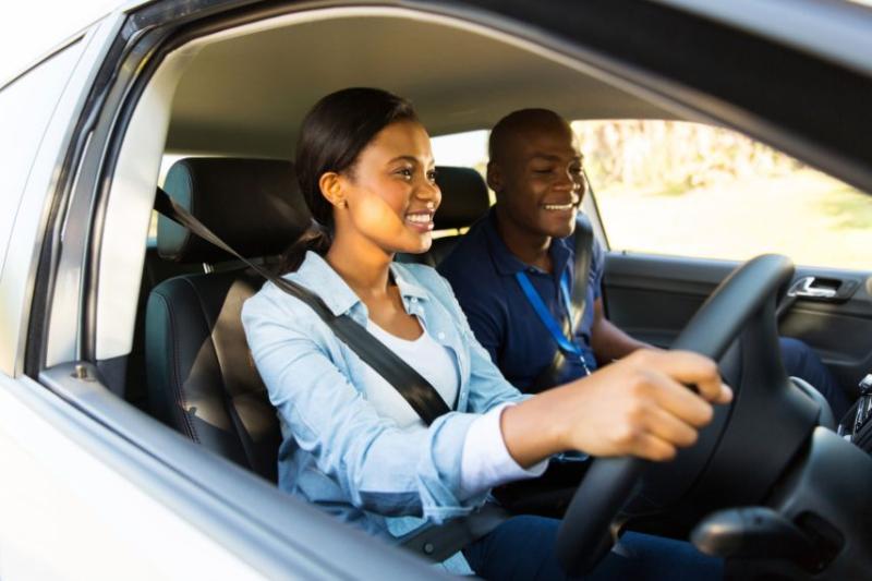 Two people in a car, one person with a lanyard teaching them how to drive