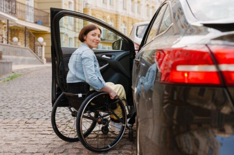 A woman in a wheelchair with a blue shirt beside an open car door