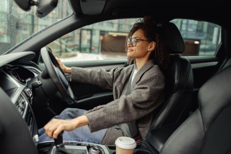 Woman in grey coat and glasses driving