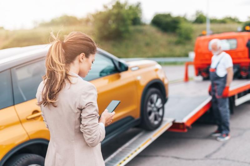 Woman on the phone standing in front of orange car being towed
