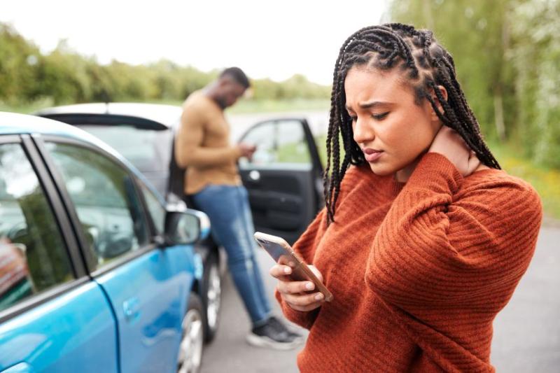 A woman looking stressed on the phone in front of a car accident