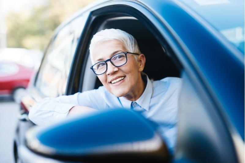 An older woman with glasses and short white hair in a car smiling