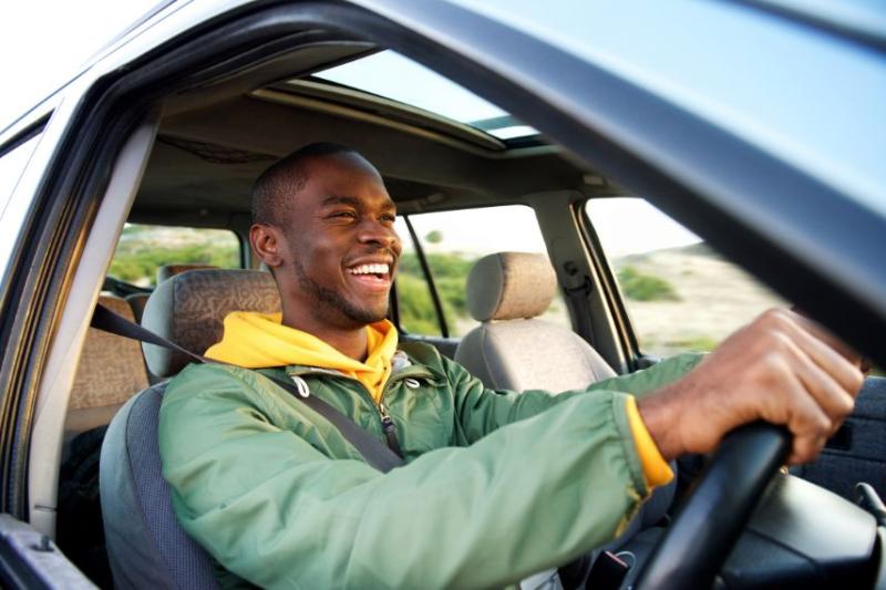 A young man in a green coat smiling and driving a car