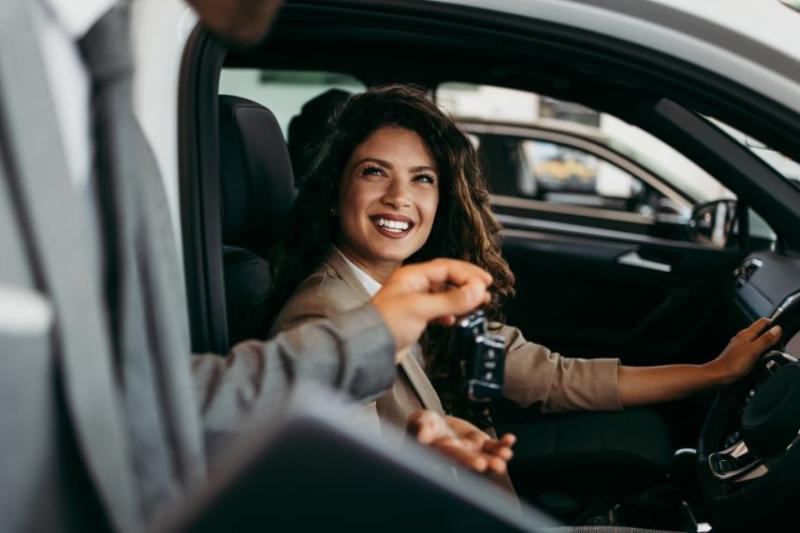 A woman sitting in a car being handed a car key