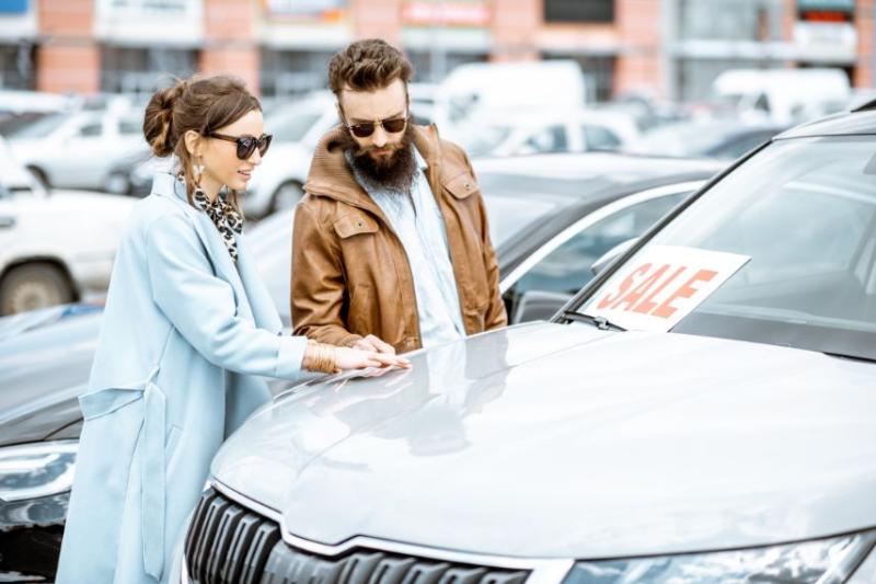 A young couple looking at a car that has a 'sale' sign on it