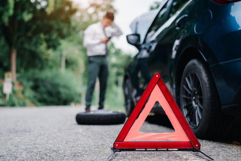 A man in a suit by a broken down car with a warning sign