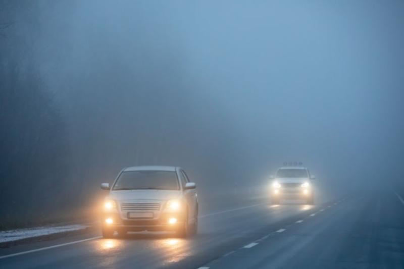 Two cars driving on a road through heavy fog