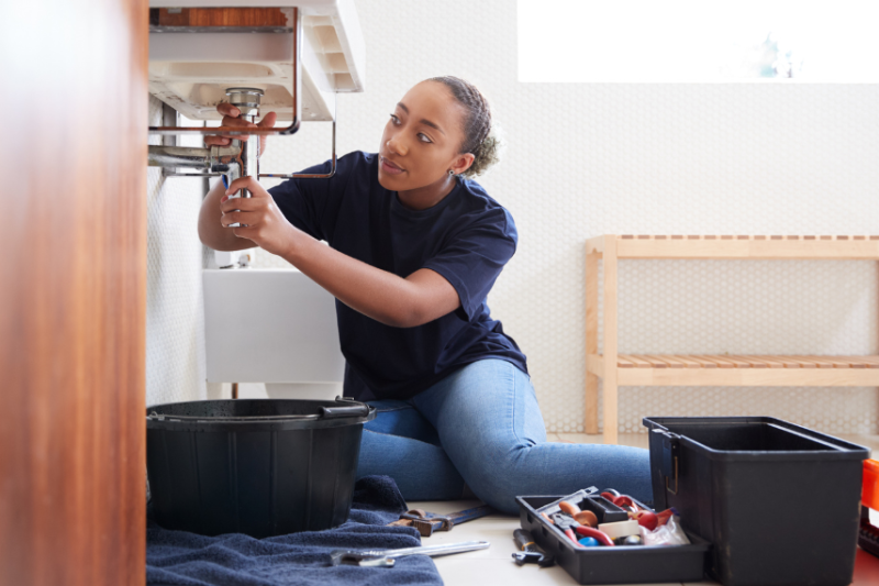 A young female plumber fixing a sink, with tools around her