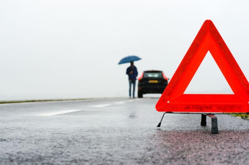 An orange triangle with a man broken down in his car in the background, with an umbrella