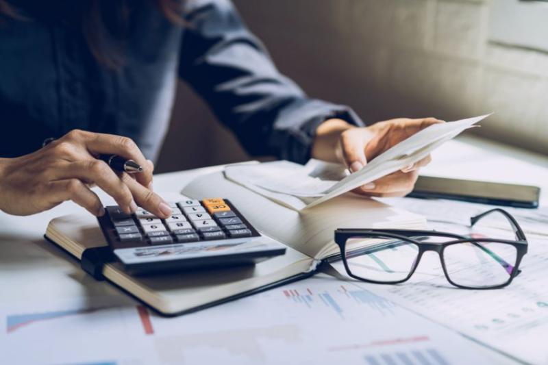 Two hands with a calculator and a bill, and a pair of glasses on the table