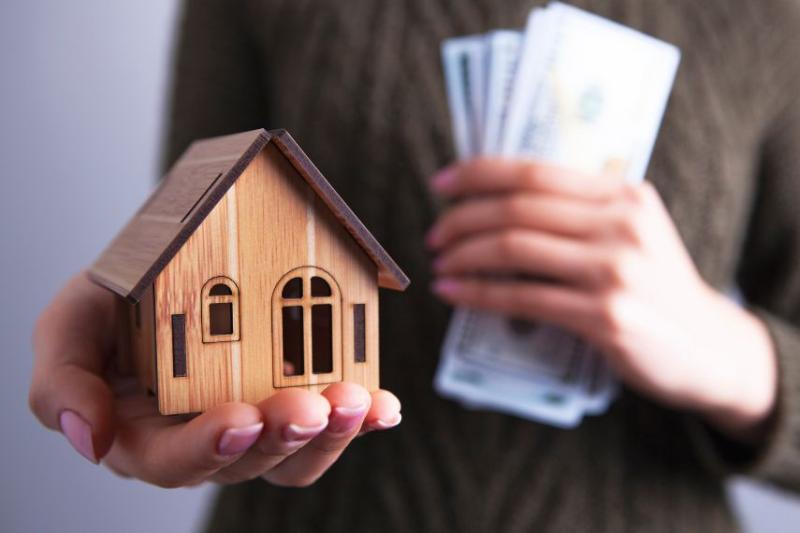 person holding house figurine and money