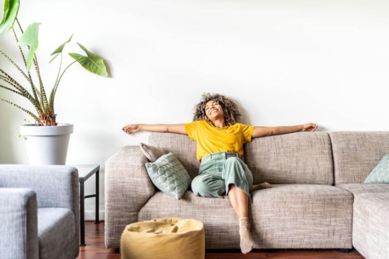 A woman in a yellow top leaning back on a beige sofa, smiling