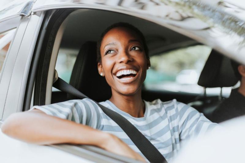 A happy, smiling woman in the driver's seat of a car
