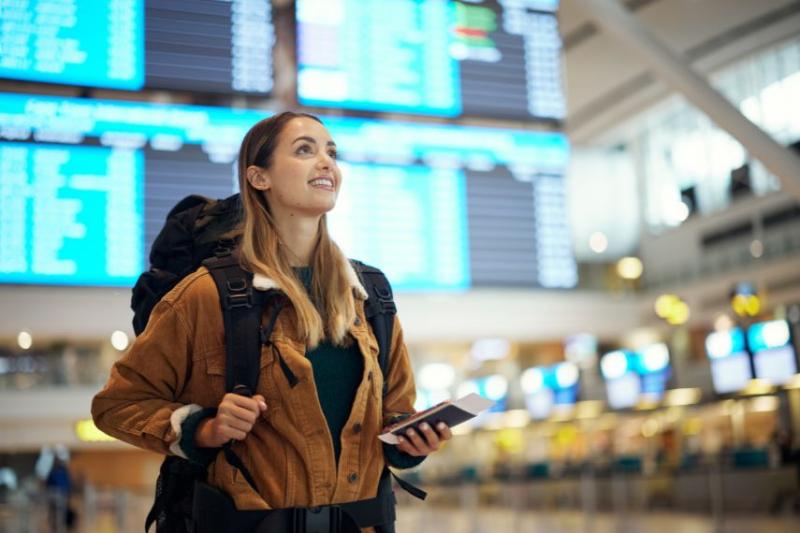 A woman in airport with a backpack on, holding her passport and smiling