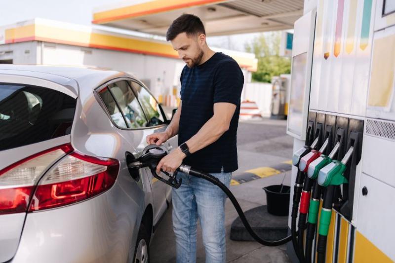 A man in a black t shirt filling his car up at a petrol station
