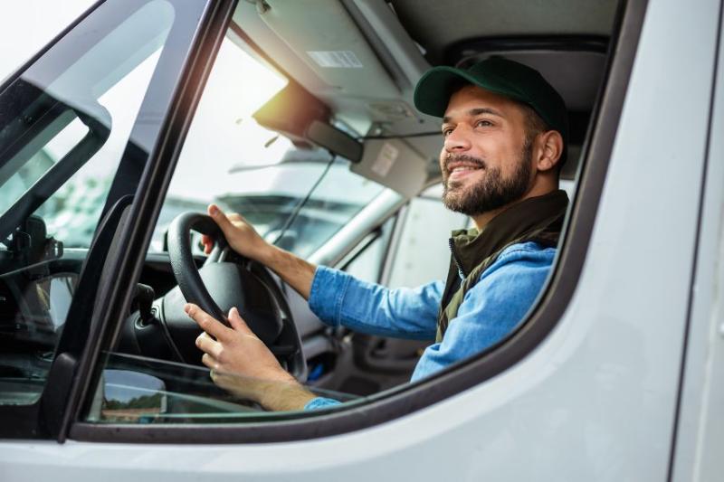 A man in a blue shirt wearing a cap driving a van