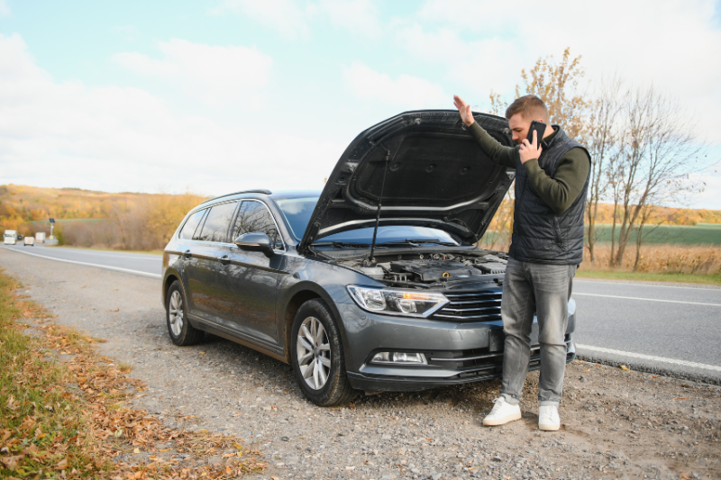 man on side of road looking under car bonnet