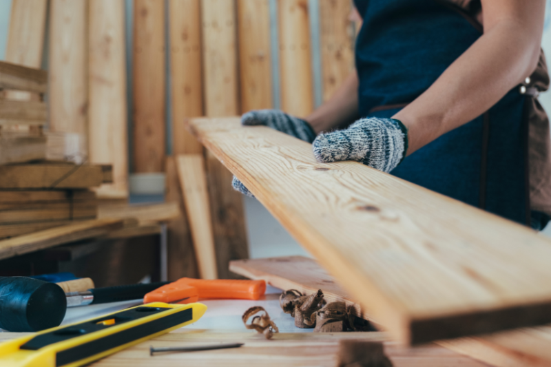 person picking up wood plank next to tools