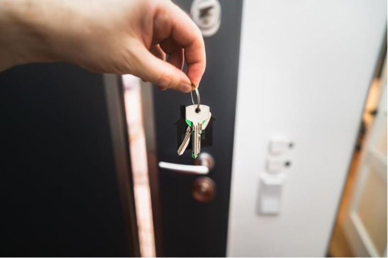 Someone holding a house key on a key chain in front of a black door
