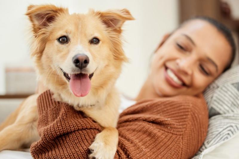 A smiling woman in an orange cardigan hugging her tan and white dog