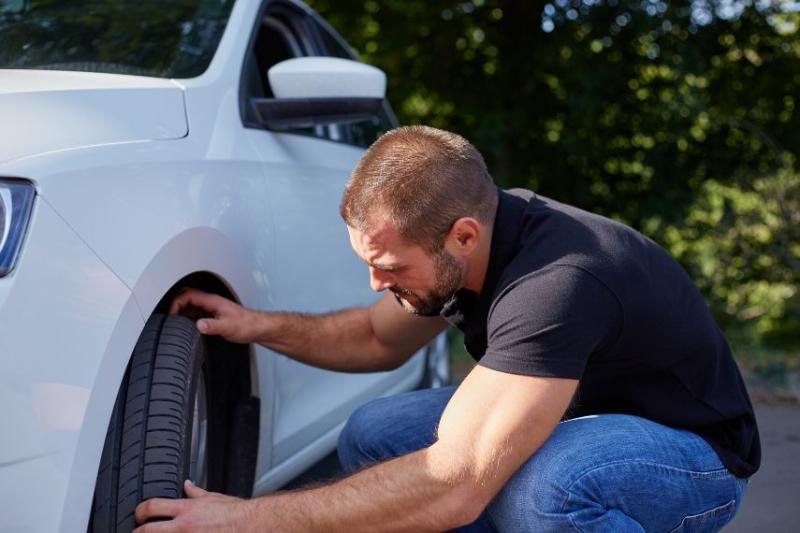 A man leaning down checking the tyres on a white car