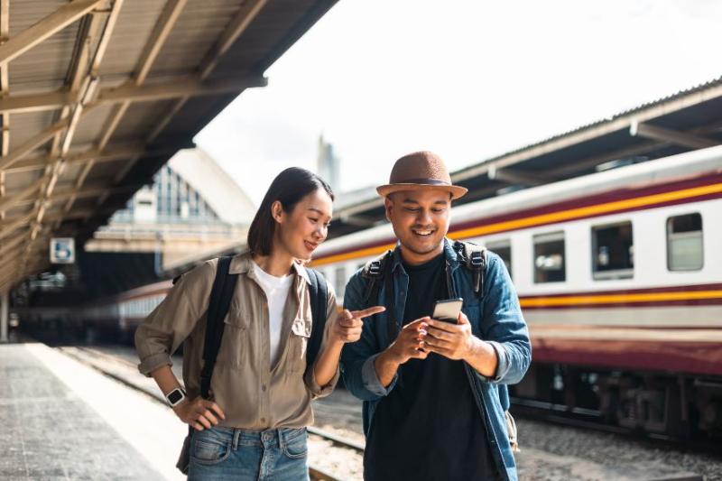 A young couple standing in a train station smiling and looking at one of their phones