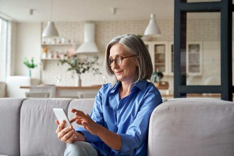 A mature woman sitting on a grey sofa in her house on the phone