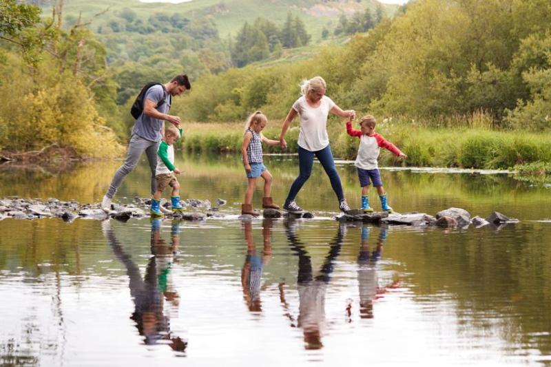 A mother and father with three young children crossing stepping stones across a river in the Lake District, UK
