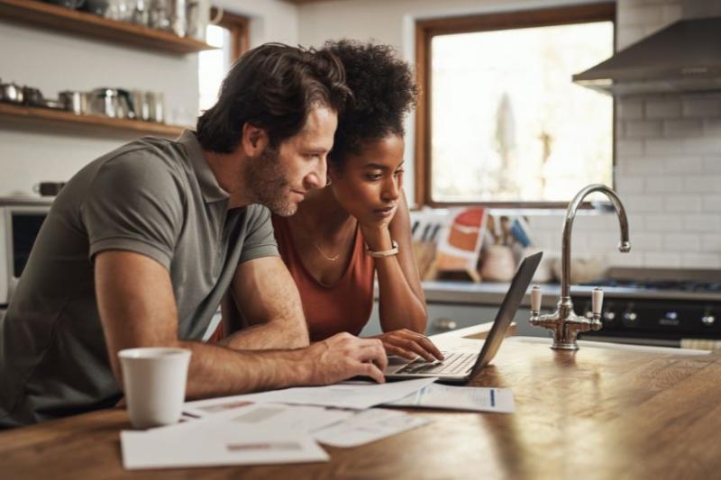 A couple standing a kitchen island looking at a laptop with some paper spread in front of them