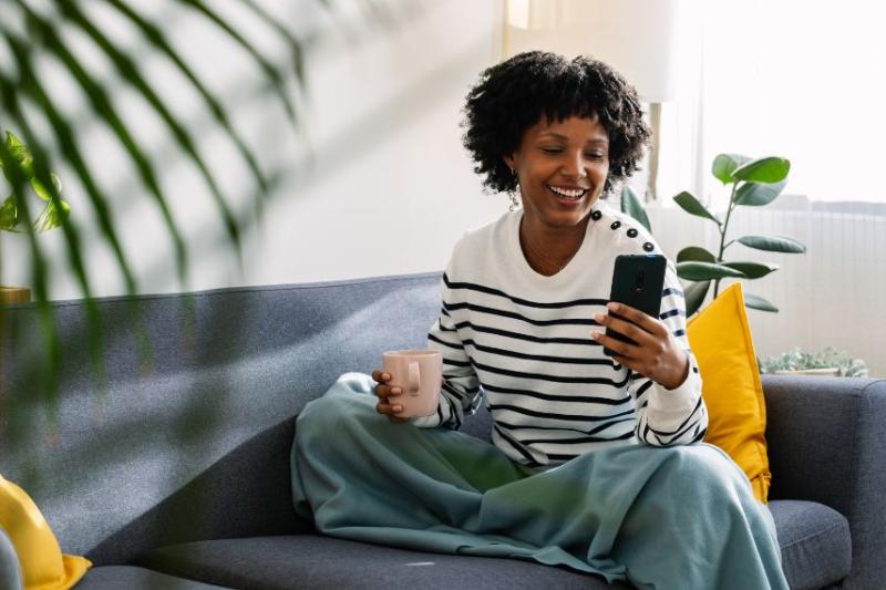 A woman sat on the sofa looking at her phone and smiling